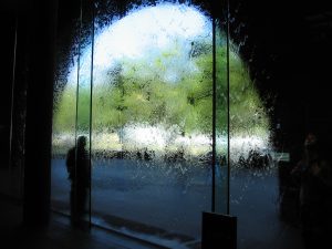 One blurred figure stands against wall of water on a glass window provides an interesting view of the world outside.