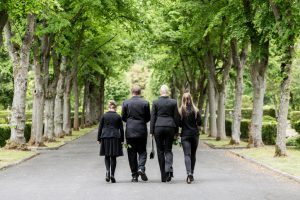Rear view of family dressed all in black walking down cemetery path with roses