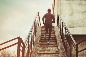 Rear view of athletic person of color wearing workout clothing and running up and down stairs outside older building 