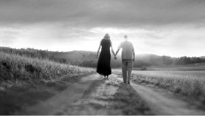 Black and white photo of couple walking into distance along trail holding hands 