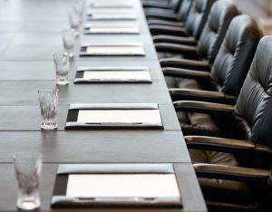 Long table with several chairs pushed in, notepads and glasses of water set for each person