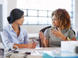 Two colleagues sit at a table to have a discussion in an office