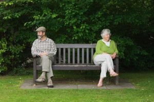 Senior couple on opposite ends of a park bench, appearing to ignore each other. 