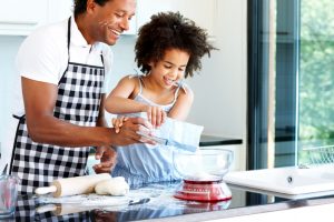 Father and child of 6-8 years wear aprons and prepare a meal in the kitchen together smiling