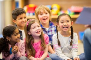 A multi-ethnic group of elementary-school-age children are listening to their teacher read a storybook in class.