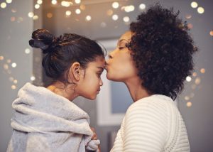 Mother kisses forehead of child who has serious expression and is wrapped in a towel after a bath