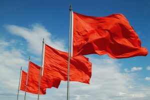 A row of red flags blowing in the wind against a blue sky with scattered clouds