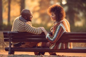 Couple sits on bench, turned toward each other, conversing deeply. Body language relaxed