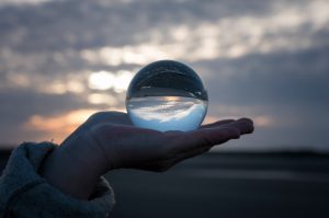 Image of a hand holding a glass globe with reflections of a sunset inside it.