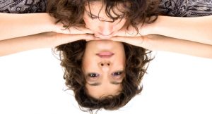 Person with curly long hair looks down into mirrored table. Reflection looking up is somewhat distressed