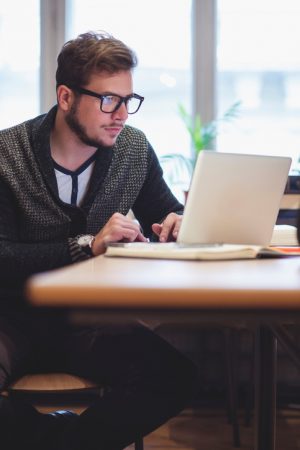 Person with large glasses, beard, and short hair uses computer to do research