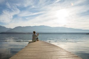 Person sitting on end of pier at lake reading a book