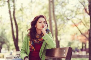 Thoughtful person with long curly hair rests head on hand on bench in the park