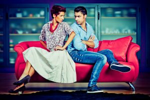 Young couple in conflict face off on fuchsia sofa. Room is done in bright colors. 