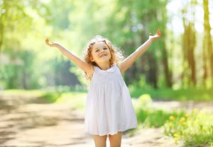 Young child with long blonde hair stretches arms up happily