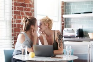 Happy couple looks at each other, leaning in close to kiss in front of open laptop