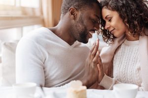 A couple looking at each other lovingly in white blankets in bed touches palms. smiling at each other