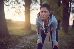Person with shoulder-length hair pulled back, standing bent, holding knees and resting after jogging on the riverside