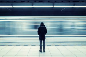 Lonely young man shot from behind at subway station with blurry moving train in background