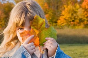 Focus on child with long hair peeking out from behind green and orange large leaf