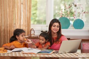 Cheerful but busy mother works on laptop while taking care of two children