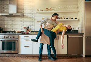 Young couple in kitchen. One partner bends back the other partner playfully