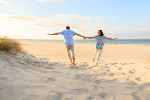 Rear view distance photo of couple holding hands leaning apart while running through sand on beach