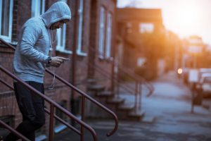 Young adult in light gray hoodie heads down steps holding music player to go on run