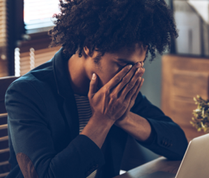 Person sits at desk with hands over face looking stressed