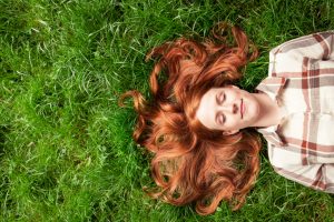 Person with long red hair lies in grass, hair spread out around 