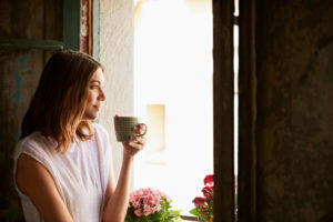 Shot of a young woman drinking a cup of coffee while looking out of a window