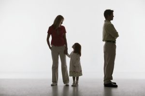 One parent holds hand of child looking up trustingly while other parent faces other direction, arms crossed