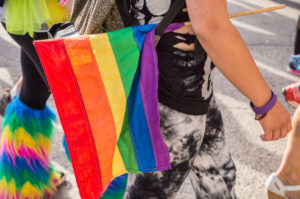 Side view of a person holding Pride flag at parade walking with others