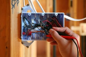 Hand using tool works to test wires in circuit switch box