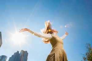 Person in gold dress with long hair stretches arms out, spinning under blue sky