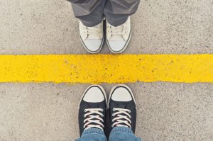 Two pairs of feet facing each other from opposite sides of yellow line on sidewalk