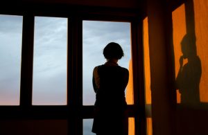 Person in shadow looking out high window into cloudy sky