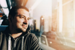 Adult with close-cropped dark hair looks out train window in contemplation while traveling through city