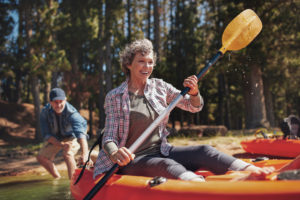 Portrait of happy senior paddling kayak in the lake with man supporting from behind. Mature couple enjoying a day at the lake.