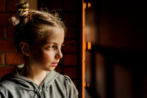 young child with hair up in pigtails looks off to the side in dimly lit room with a serious expression