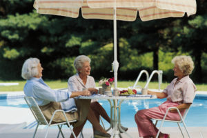 Three mature adults with short hair sit at decorated table by pool enjoying coffee