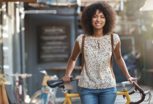 Young adult with curly hair stands in front of bike facing camera with smile