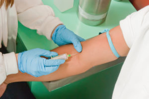 Cropped view of gloved tech's hands about to draw blood from forearm of patient