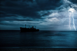 Cargo ship sails across darkening sea with lightning against the sky