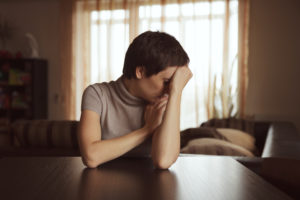 Upset person covers face with hand, leaning to one side, sitting at kitchen table