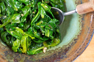 Spoon rests in bowl of fresh spinach 