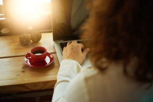 Rear view of person with curly hair using laptop next to coffee cup