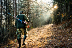 Man with hunting rifle walking through woods