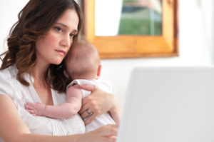 Mother holding baby while looking at computer