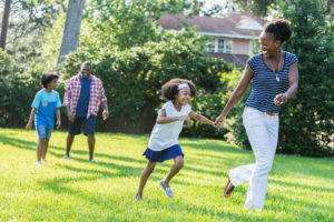 Family with two children run playfully together across suburban lawn